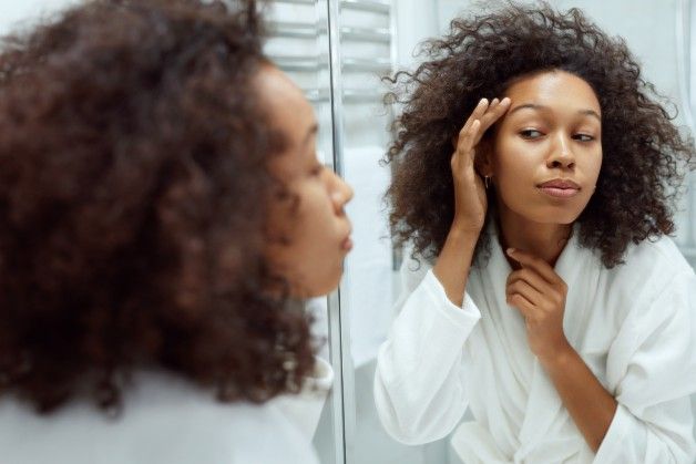 Woman applying skincare in bathroom mirror.