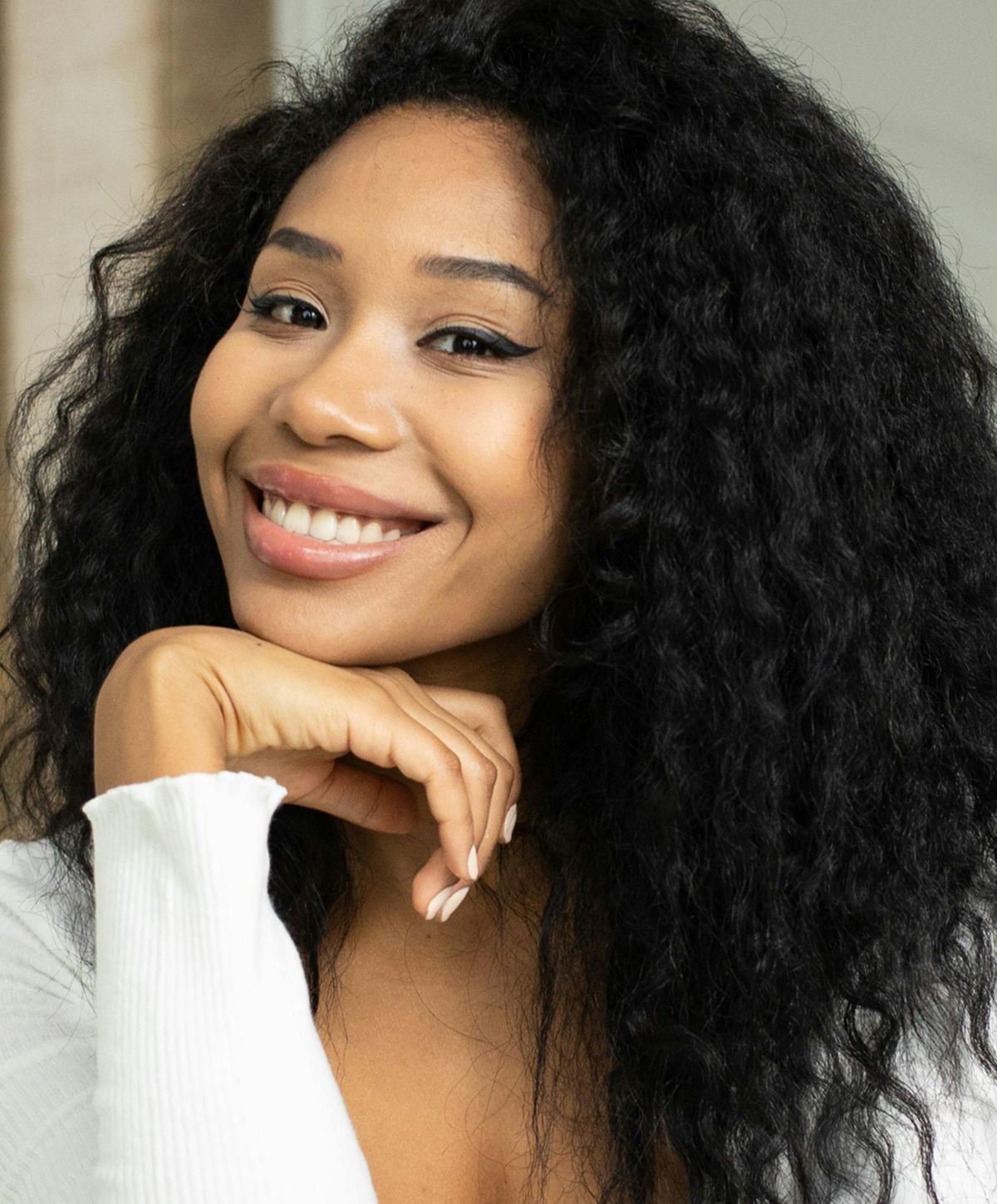 Smiling woman with curly hair, hand on chin.