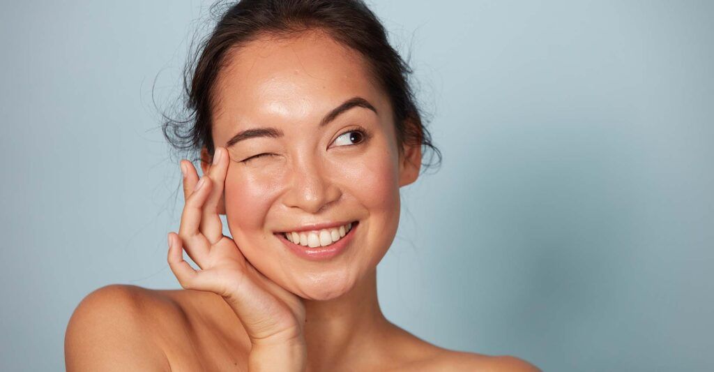 Woman winking and smiling against a blue background.