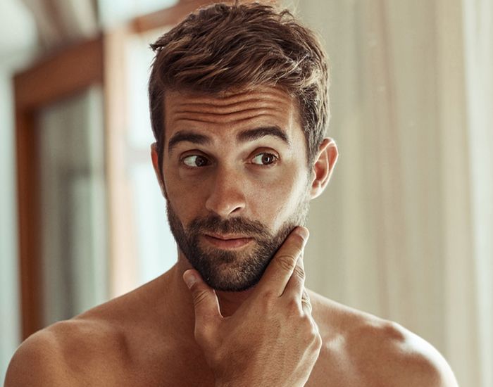 Man thoughtfully touching his beard in mirror.